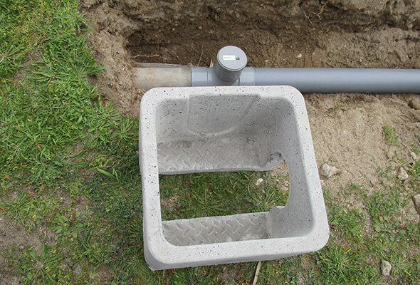 Pose d'un regard d'évacuation en béton et d'une canalisation en PVC dans une tranchée.